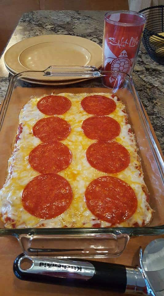 Guten-Free Flourless Pizza with Large Pepperoni Slices baked in 9 x 13 baking dish with pizza cutter, plate, and Salt Life glass beside it.