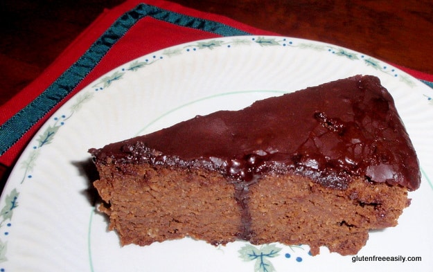 Single slice of Double Chocolate Clementine Cake on plate with holly leaves and berries on top of red napkin trimmed in green ribbon. One of 25 gluten-free chocolate cakes on glutenfreeeasily.com.