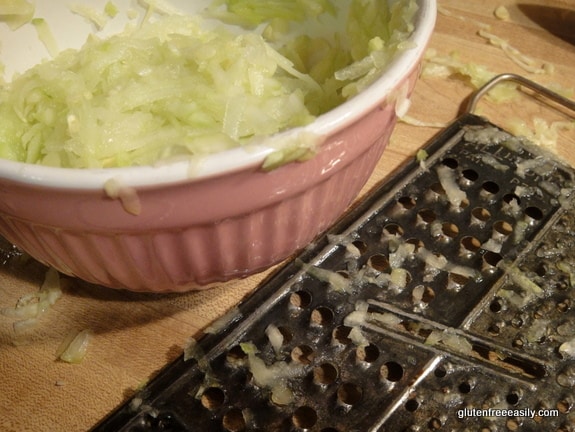 Shredded zucchini in bowl with grater. [GlutenFreeEasily.com]