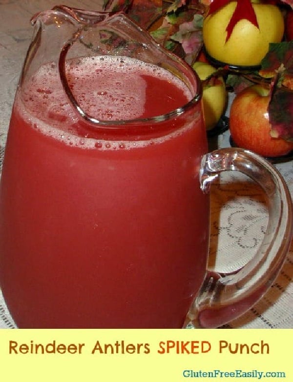 Reindeer Antlers Punch, the perfect holiday cocktail, in a glass pitcher beside apples in wrought iron centerpiece on cut-lace tablecloth.