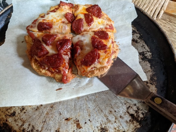 Six-Inch Gluten-Free Individual Pizza Made using almond flour, tapioca flour and coconut flour cut into four pieces on parchment paper on an old pizza pan with spatula.