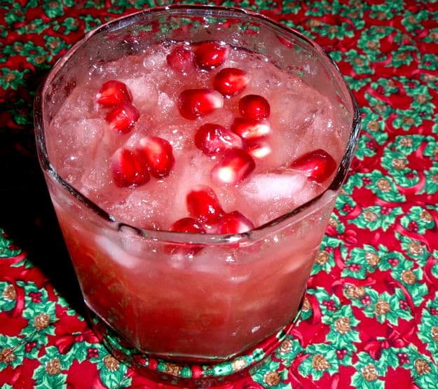 Reindeer Antlers Punch, the perfect holiday cocktail, in a highball glass topped with pomegranate seeds (arils) on a quilted Christmas placemat.