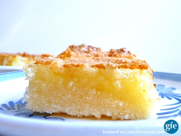 A single lemon bar on a white and blue plate with more gluten-free lemon bars in the background.