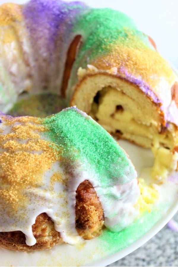 Gluten-Free King Cake from She Let Them Eat Gluten-Free Cake with slice removed on white cake platter.