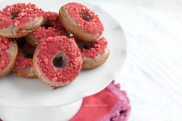 A pile of donuts with bright pink strawberry topping on a raised white platter.