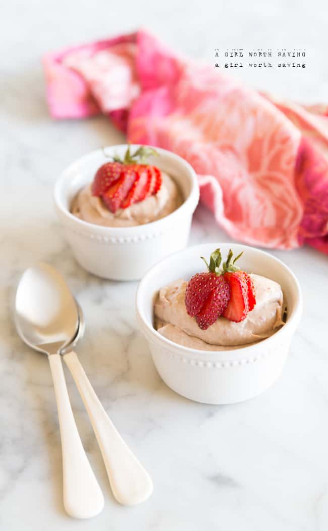 Two white ramekins filled with strawberry mousse topped with strawberry slices and two spoons on the side.