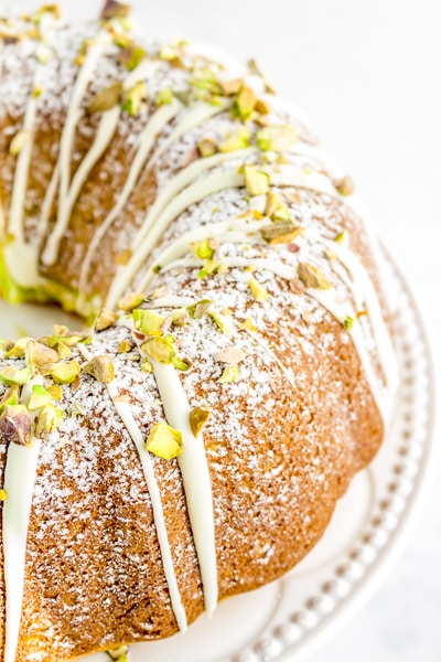 Half of a gluten-free pistachio cake sprinkled with frosting and chopped pistachios.