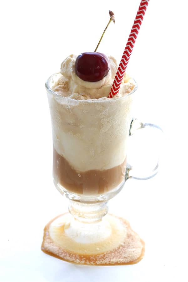 A glass mug filled with a Keto Low-Carb Root Beer Float topped with whipped ream and a cherry with a red-and-white striped straw.