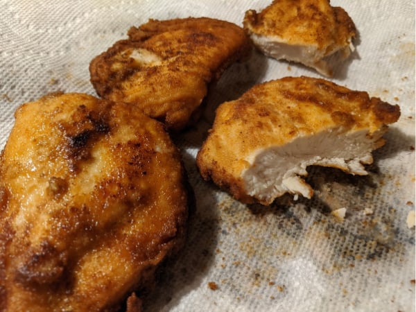 Perfect Gluten-Free Fried Chicken Breasts draining on paper towels with one cut in half so you can see the inside.