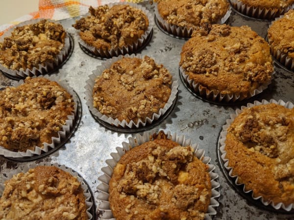 Close-up of gluten-free and paleo Apple Crumb Muffins in old Ecco muffin tin cooling on plaid cotton dish towel.