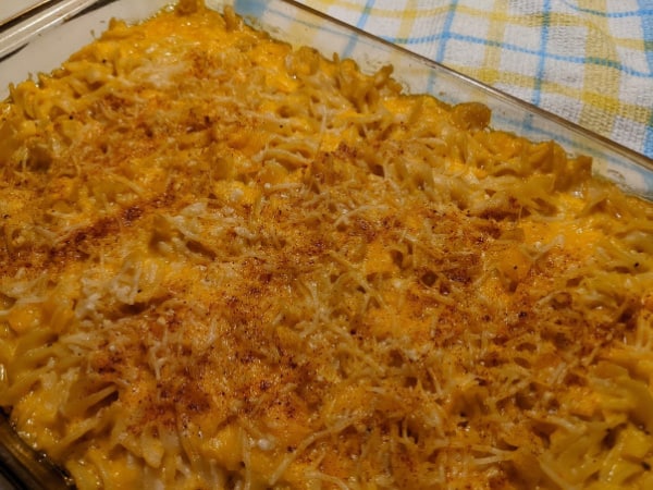 A 9 x13 baking dish of Extra Cheesy Gluten-Free Macaroni and Cheese sprinkled with paprika placed on a yellow and blue plaid dish towel.