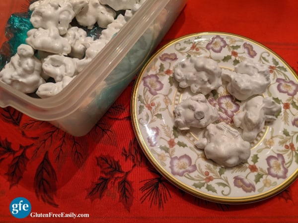 Naturally gluten-free Forgotten Cookies nestled in green plastic wrap in a Tupperware bread container sitting on a holiday tablecloth.