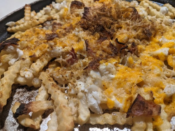 Gluten-Free Crab Fries with Cheese and Bacon. Shredded cheese, lump crab meat, bacon, and Old Bay seasoning top French Fries on a well-worn round baking sheet.