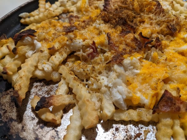 Gluten-Free Crab Fries with Cheese and Bacon. Shredded cheese, lump crab meat, bacon, and Old Bay seasoning top French Fries on a well-worn, round baking sheet.