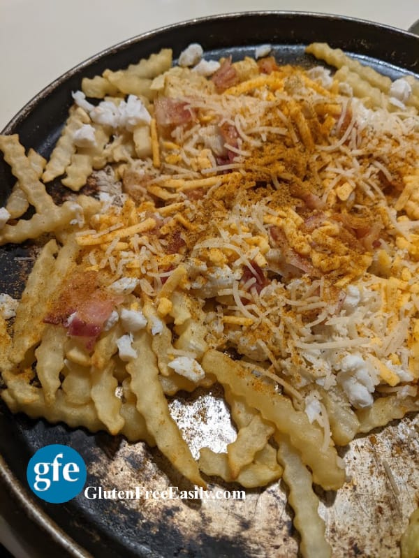 Gluten-Free Crab Fries with Cheese and Bacon. Shredded cheese, lump crab meat, bacon, and Old Bay seasoning top French Fries on a well-worn round baking sheet.