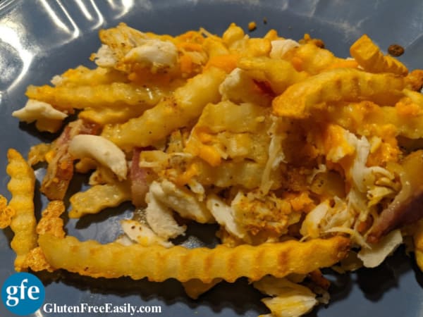 Gluten-Free Crab Fries with Cheese and Bacon. Shredded cheese, lump crab meat, bacon, and Old Bay seasoning top French Fries on a blue dinner plate.