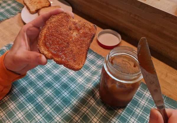 Crockpot Apple Butter made from applesauce spread on a slice of gluten-free toast with a half empty canning jar of the apple butter nearby.