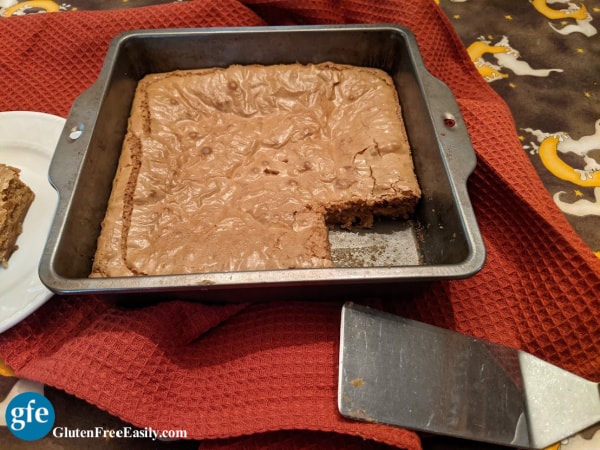 Gluten-Free Caramel Squares in baking dish with one square missing and one corner square with wonderfully chewy edges on a white plate.