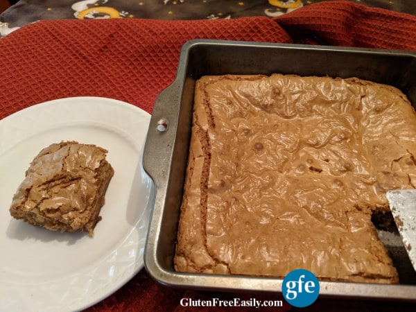 Gluten-Free Caramel Squares in baking dish with one square missing and one corner square with wonderfully chewy edges on a white plate.