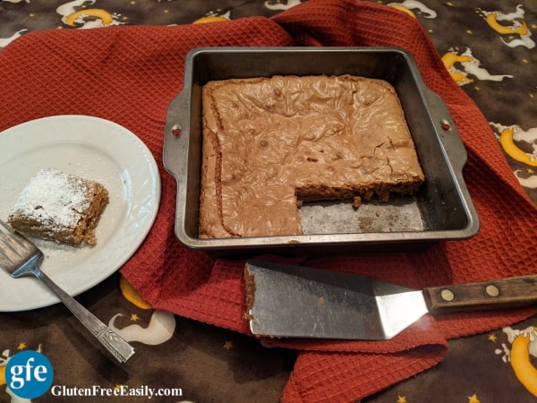 Gluten-Free Caramel Squares in baking dish with two squares missing and one corner square dusted with powdered sugar on a white plate.