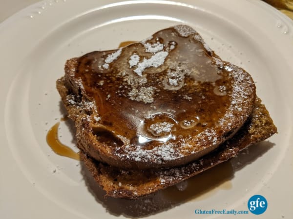 A single serving of Gluten-Free Overnight Pumpkin Pie French Toast Casserole with powdered sugar and maple syrup on a white plate.