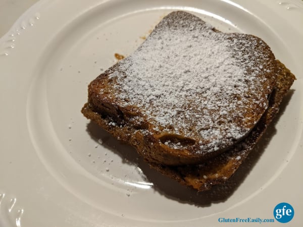 A single serving of Gluten-Free Overnight Pumpkin Pie French Toast Casserole with powdered sugar on a white plate.
