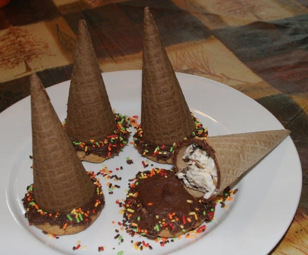 Gluten-Free Hocus Pocus Cookies with one cookie broken open to show ice cream-filled cone on iced peanut butter cookie with sprinkles a white plate on Fall checkered tablecloth.