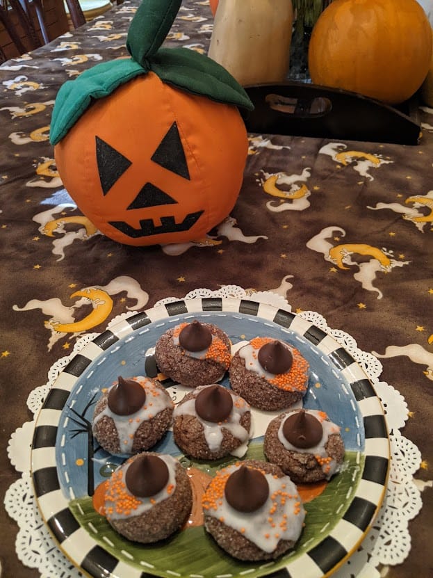 Gluten-Free Witch Hat Cookies on Halloween plate on white doily on Halloween ghost tablecloth with stuffed Jack-o-lantern and fresh pumpkins and squash behind it.