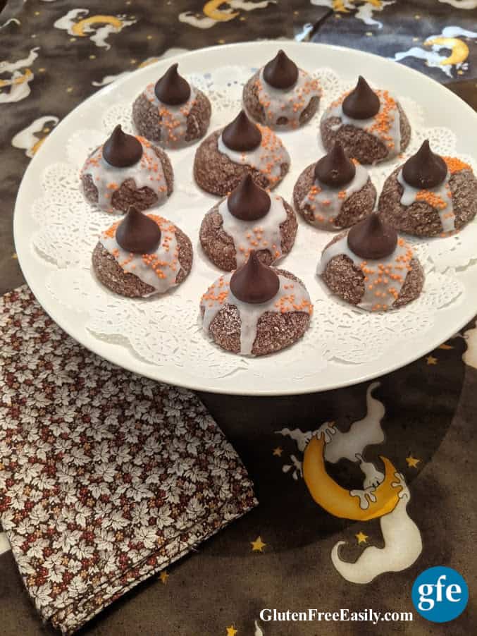 Gluten-Free Witch Hat Cookies on doily on white cake stand on Halloween ghost tablecloth with Fall leaves napkin.