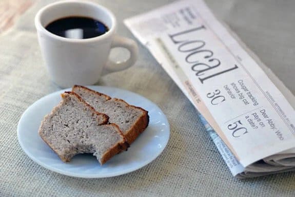 Gluten-free and paleo Banana Bread from Elana's Pantry. Two slices on white plate next to mug of coffee and folded newspaper.