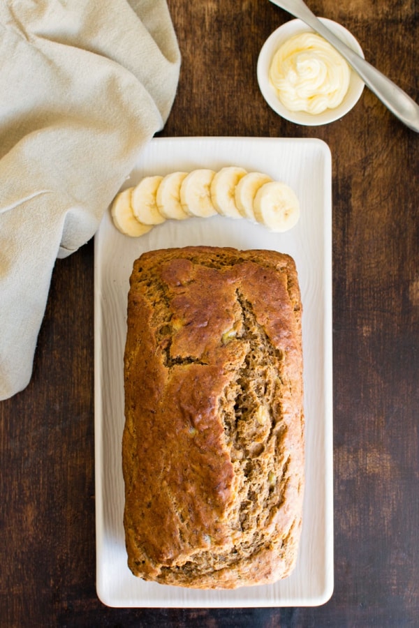 Breakfast-Worthy Banana Bread (with gluten-free option) from Go Dairy Free. Loaf on long white platter with sliced bananas at the end. One the best gluten-free banana bread recipes featured on gfe.