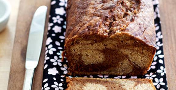 Gluten-Free and Allergen-Free Banana Chocolate Swirl Bread from Cybele Pascal. Loaf on black and white flowered napkin with one slice cut and laying on napkin. One of the gluten-free banana bread recipes featured on gfe.one of the