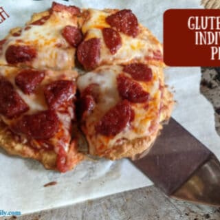 Six-inch gluten-free individual pizza (grain-free, too) cut into four slices on parchment paper on pizza pan with spatula underneath. On glutenfreeeasily.com. Made using almond flour, tapioca starch, and coconut flour. Yeast free and gum free.