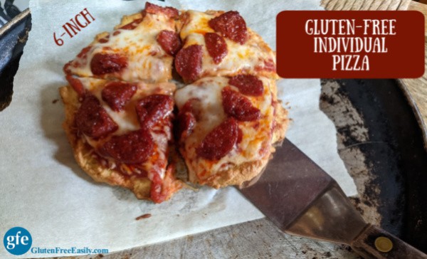 Six-inch gluten-free individual pizza (grain-free, too) cut into four slices on parchment paper on pizza pan with spatula underneath. On glutenfreeeasily.com. Made using almond flour, tapioca starch, and coconut flour. Yeast free and gum free.