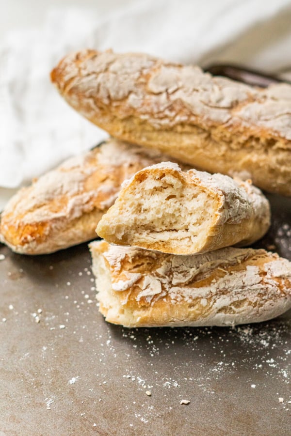 Three small gluten-free and vegan French baguettes on a baking sheet from Vibrantly G-Free. One of the gluten-free French Bread recipes featured on gfe.