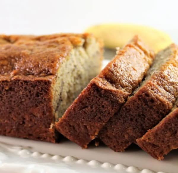 The best gluten-free banana bread from Let Them Eat Gluten-Free Cake. One of the best gluten-free banana bread recipes featured on gfe. Loaf on white platter, partially sliced in thick slices.