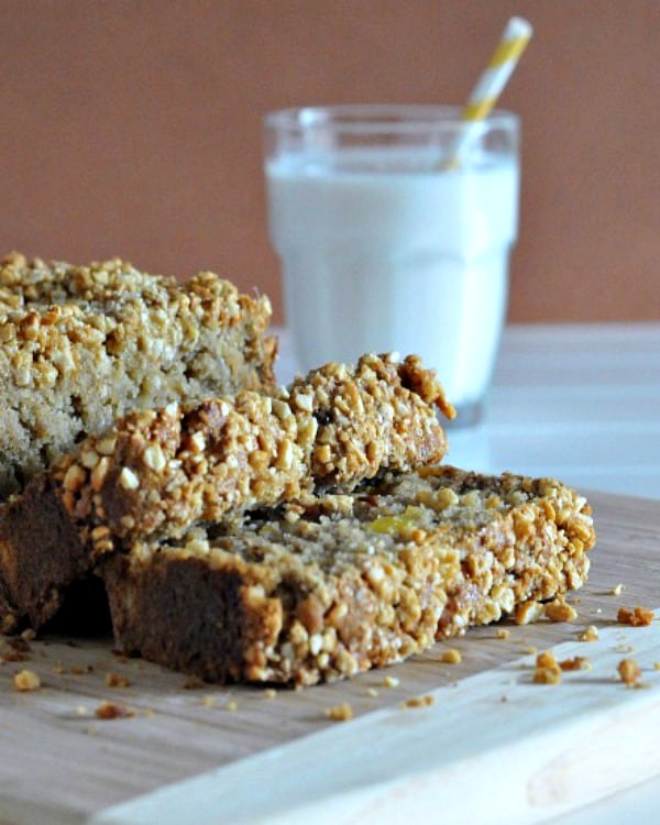Gluten-Free Tropical Banana Bread with Sugared Macadamia Crumble from Spabettie. One of the best gluten-free banana bread recipes featured on gfe. Sliced loaf of bread on cutting board with clear glass of milk with straw beside it.