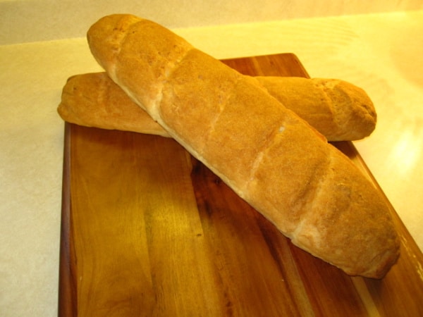 Two loaves of gluten-free French Bread, baguettes, crossed on a cutting board. One of the gluten-free French bread recipes featured on gfe.