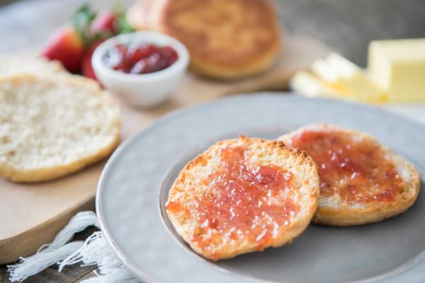 Gluten-free and paleo English Muffins from Primal Palate. One sliced and spread with jam on a plate with another behind it, plain with jam on side.