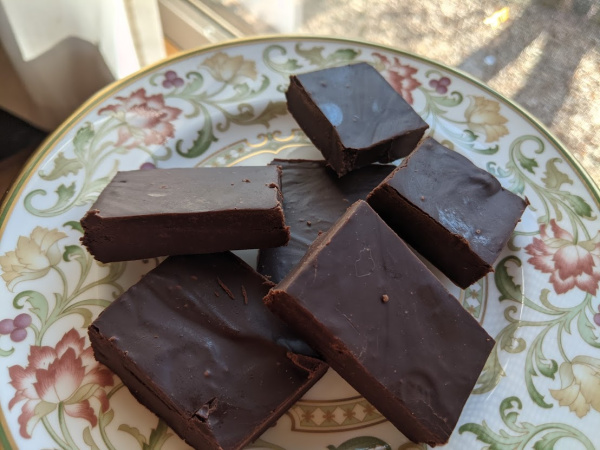 Six pieces of Dairy-Free Two-Ingredient Freezer Fudge piled on a Litchfield china bread and butter plate next to a window.