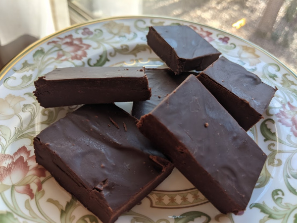 Six pieces of Dairy-Free Two-Ingredient Freezer Fudge piled on a Litchfield china bread and butter plate next to a window.