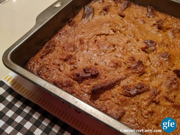Gluten-Free Pumpkin Bread Pudding in a metal 8 x 8 baking dish right out of the oven cooling on a black gingham dish towel.