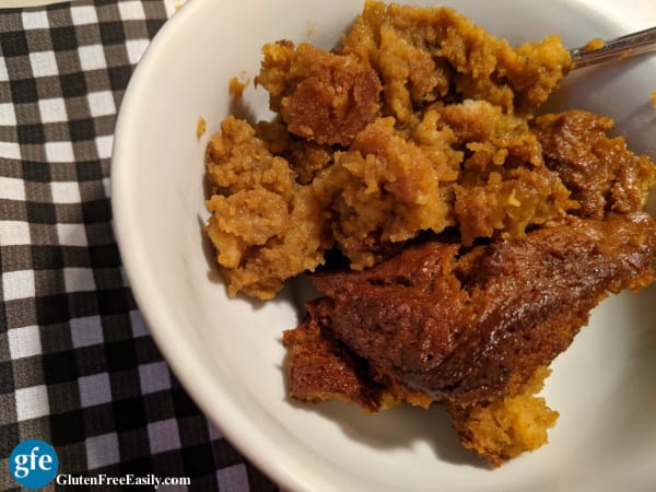 A serving of Gluten-Free Pumpkin Bread Pudding in a white bowl on a black gingham dish towel.