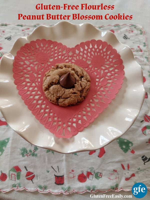 Gluten-Free Flourless Peanut Butter Blossom Cookies on elevated white ruffled dessert plate on dining room table on vintage Christmas handkerchief.