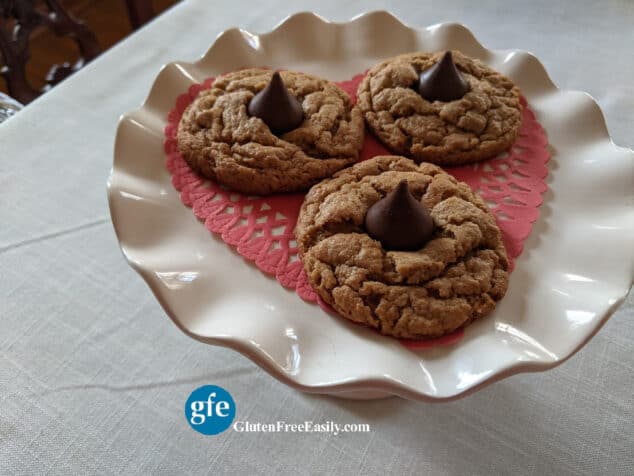 Gluten-Free Flourless Peanut Butter Blossom Cookies on White Ruffles Elevated Plate on Off White Tablecloth.