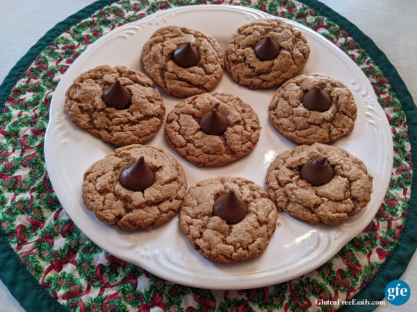 Flourless Gluten-Free Peanut Butter Blossom Cookies on a white plate with filly edges on a round holiday placemat with Christmas wreaths and dark green trim.
