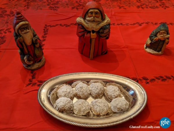 Gluten-Free Swedish Pecan Ball Cookies with Santas standing guard on a red Christmas tablecloth with poinsettias.