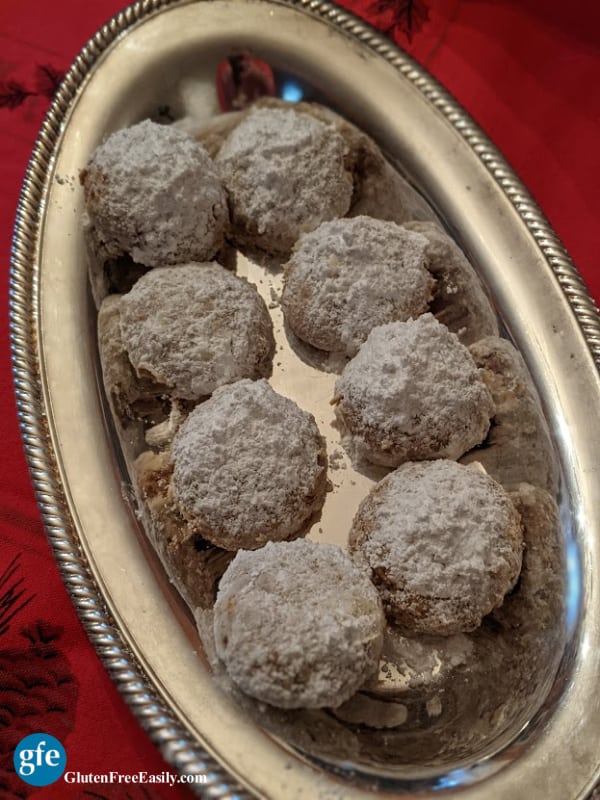 Eight Gluten-Free Swedish Pecan Ball Cookies on a silver platter on a red Christmas tablecloth.
