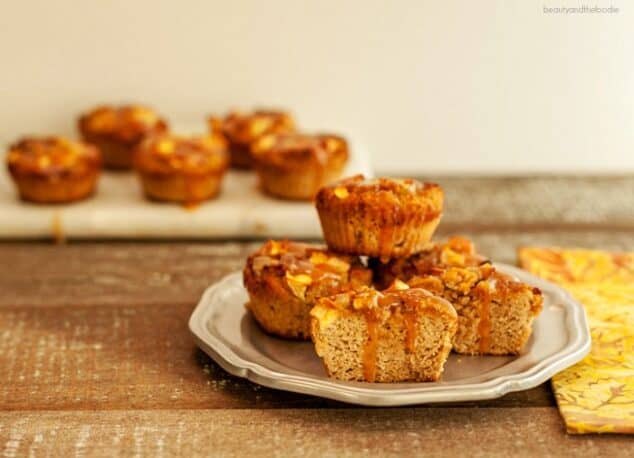 Gluten-Free and Paleo Caramel Apple Muffins from Beauty and the Foodie. Stacked on a plate in foreground and on a hand towel in background.