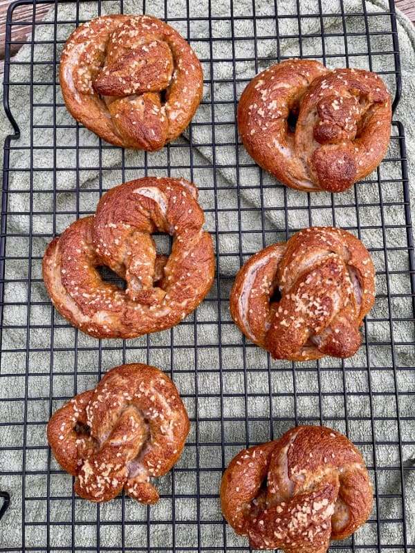 Six Gluten-Free Soft Pretzels made using Cup4Cup gluten-free flour mix cooling on a wire rack above a gray towel. From The Nomadic Fitzgeralds.